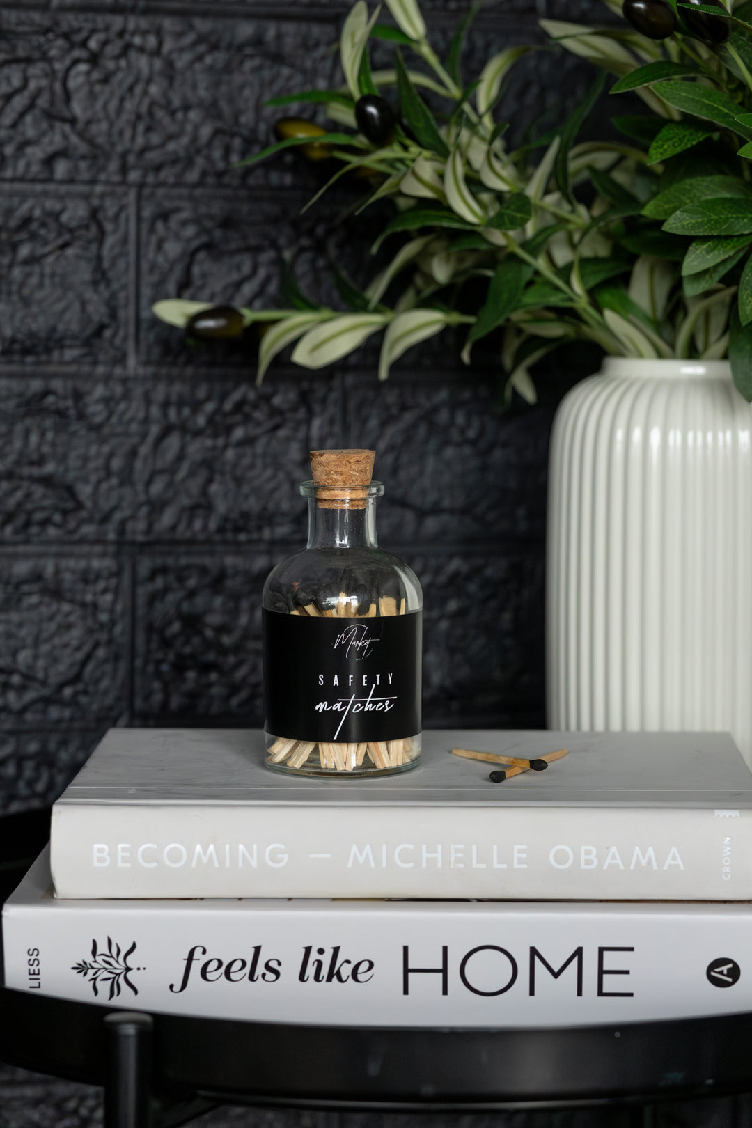Bottle with cork lid on a stack of books against a dark textured wall with a plant in the background.