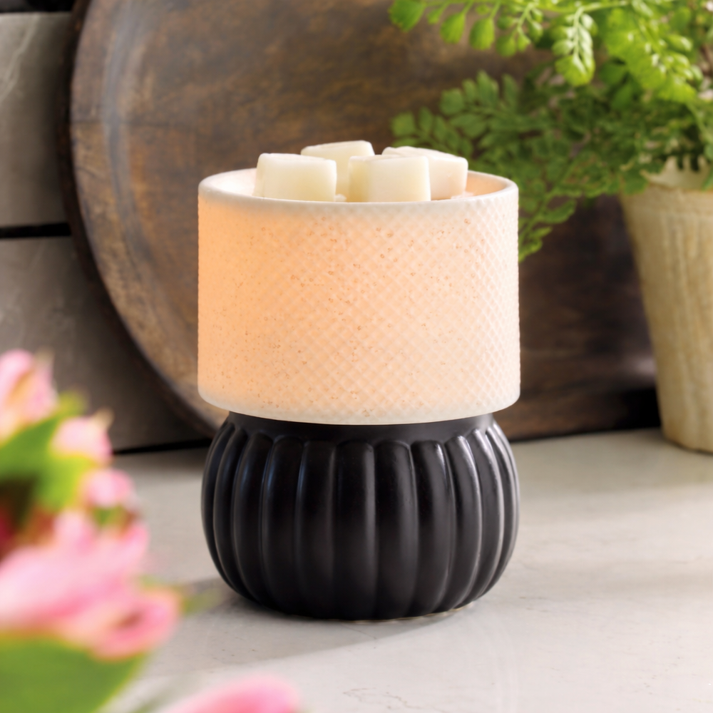 Decorative lamp with black base and beige top on a surface with blurred flowers and plant in the background