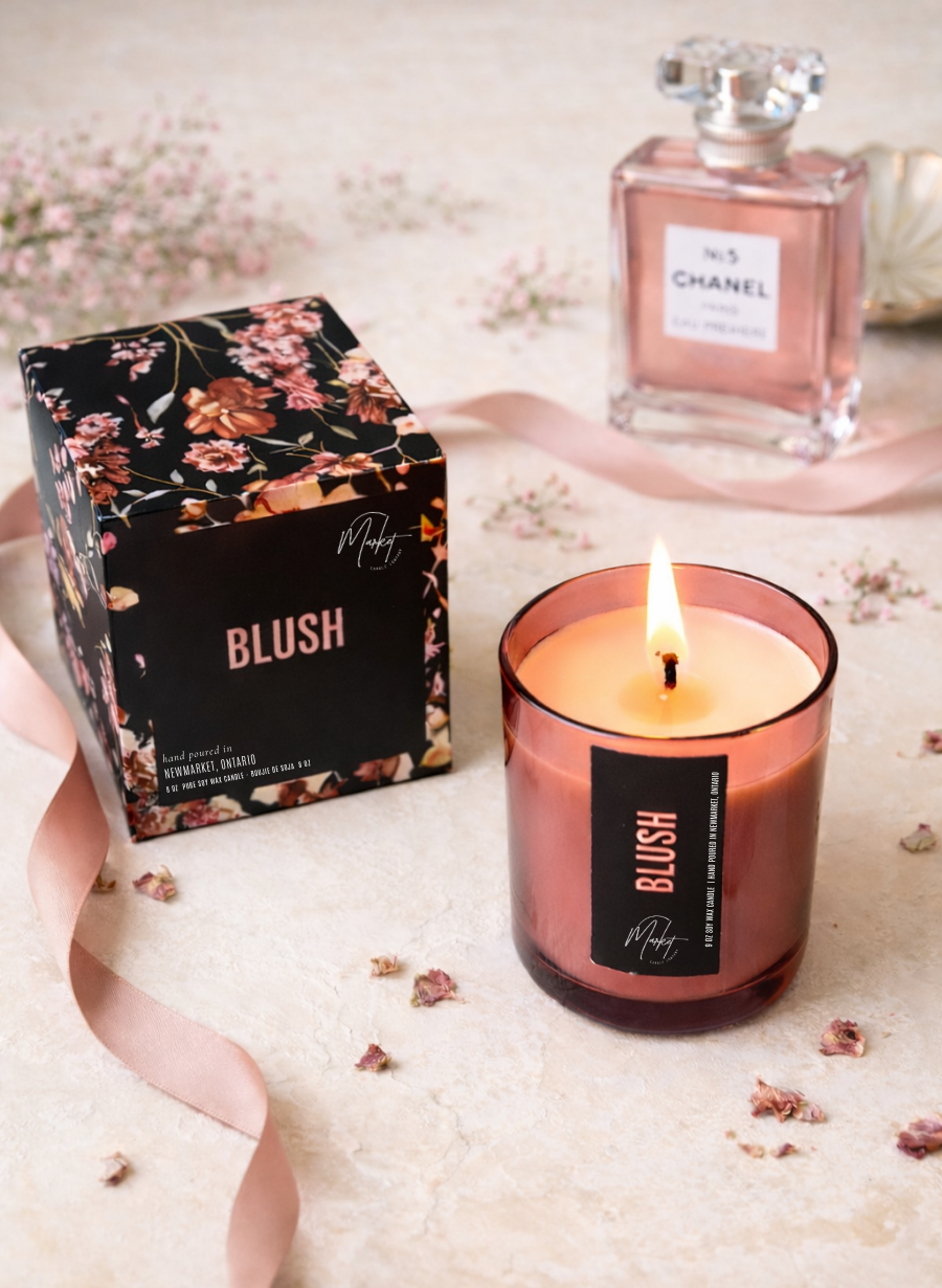 Blush-colored candle with packaging and a bottle of Chanel perfume on a light surface.
